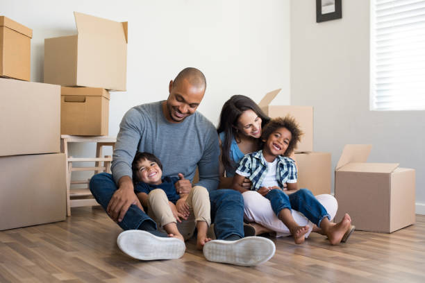 Multiethnic family moving home Happy family with two children having fun at new home. Young multiethnic parents with two sons in their new house with cardboard boxes. Smiling little boys sitting on floor with mother and dad. home insurance stock pictures, royalty-free photos & images
