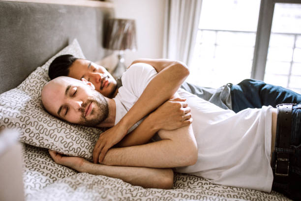 Multi-ethnic gay couple lying in bed Directly above of gay partners in bed, lying face to face and, looking each other and cuddling gay spooning stock pictures, royalty-free photos & images