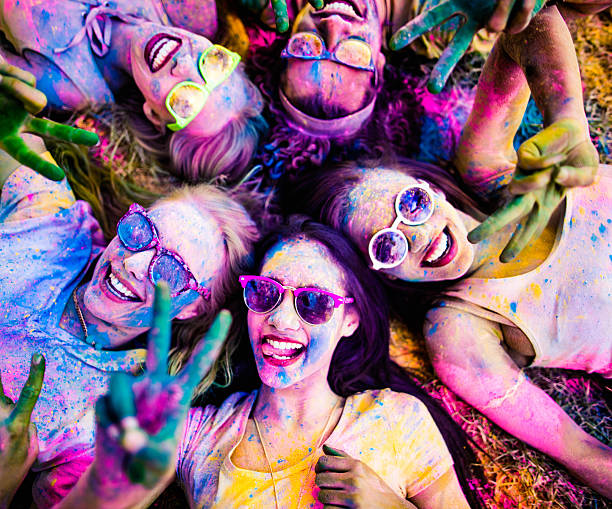 Multi-Ethnic Group Celebrating Holi Festival in Park Multi-Ethnic group covered in Holi powder lay in grass laughing and looking up and gesturing peace sign to the camera in a park at a Holi festival in the summer holi photos stock pictures, royalty-free photos & images