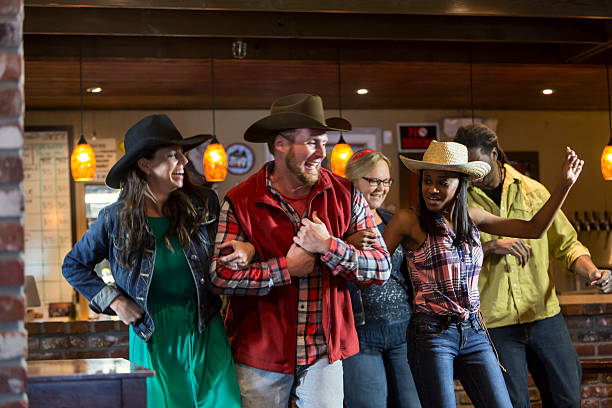 Multi-ethnic group of friends dancing in a bar A multiracial group of friends dancing in a restaurant bar, smiling and having fun.  They are wearing cowboy hats and jeans so the party has a country western theme. country and western music stock pictures, royalty-free photos & images