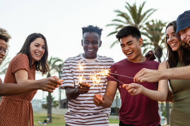 Multiethnic happy young friends having fun holding sparkles at festival eve stock photo