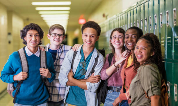 Multi-ethnic high school students hanging out in hallway A multi-ethnic group of six high school students, 15 to 18 years old, hanging out together in the hallway by the lockers, between classes. There are three teenage boys and three teenage girls, smiling at the camera. high school student stock pictures, royalty-free photos & images