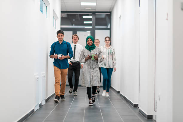 Multi-ethnic startup business team walking through the hallway of the building while coming back from a coffee break stock photo
