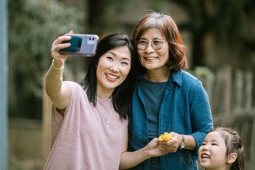A beautiful Korean family consisting of mother, daughter, and granddaughters, take a self portrait together outdoors.  They smile and laugh, having fun spending time with each other.