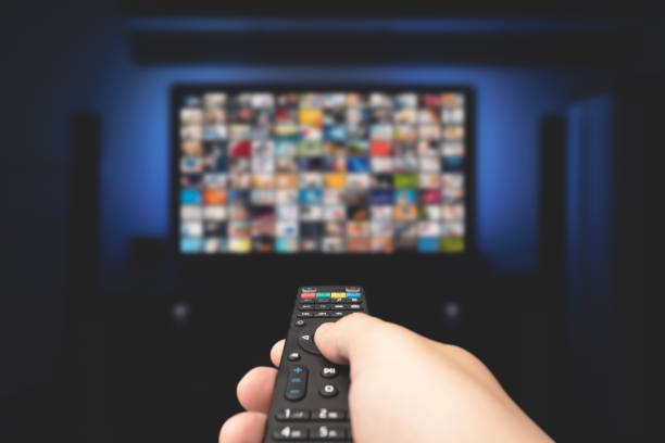 Multimedia video concept on TV set in dark room Multimedia video concept on TV set in dark room. Man watching TV with remote control in hand. television industry stock pictures, royalty-free photos & images