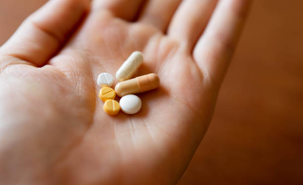 Multiple medications, including pills and capsules, in the palm of the patient's hand. stock photo