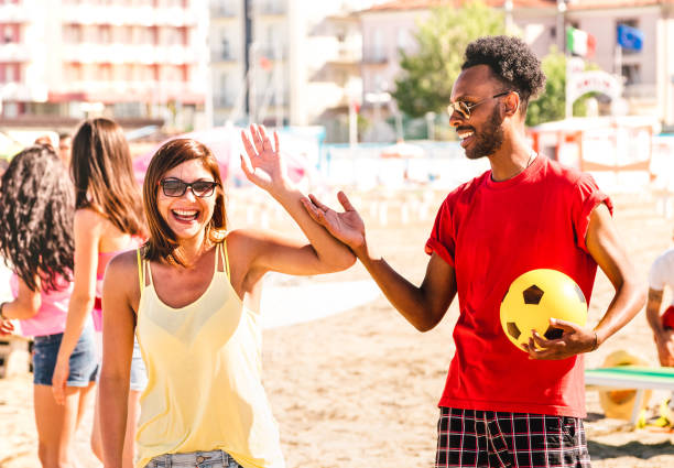 multiracial couple ready to play beach soccer on sunny day - summer vacation concept and multi cultural friendship with guy and girl having fun together - bright warm filter with focus on right man - futebol de praia imagens e fotografias de stock
