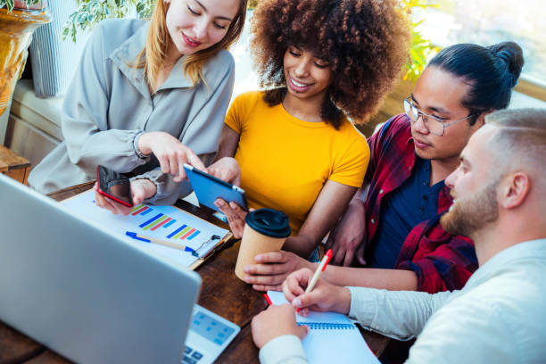 Multiracial diverse coworkers using tablet device on creative office - College students with laptop while sitting at table - Group study for school assignment  generation z stock pictures, royalty-free photos & images