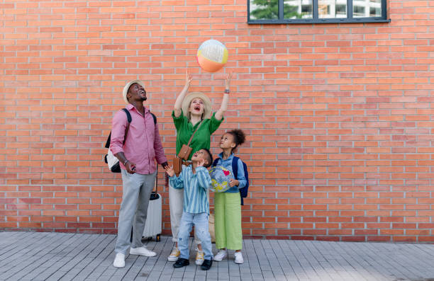 Multiracial family travelling together with small kids. Posing with beach ball in front of brick wall. stock photo