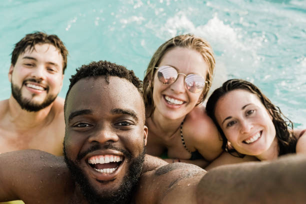 Multiracial friends at pool party taking a selfie with mobile phone - Millennials having fun during summer vacation - Focus on african american man face stock photo