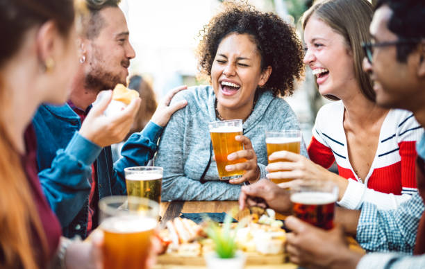 Multiracial friends drinking beer at brewery pub garden - Genuine friendship life style concept with guys and girls enjoying happy hour food together at open air bar dehor - Warm vivid filter stock photo