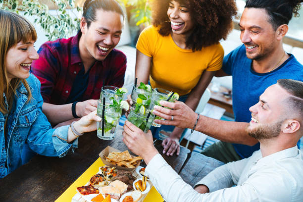 Multiracial friends enjoying happy hour toasting fresh mojito cocktails at open bar - Young people having fun celebrating at backyard home party - Focus on glasses stock photo