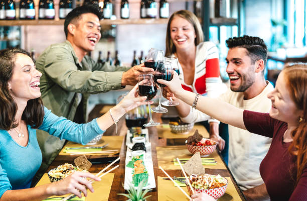Multiracial friends toasting red wine at sushi restaurant - Food and beverage lifestyle concept with happy people having fun together at fusion bar venue - Warm neon filter with focus on glasses stock photo