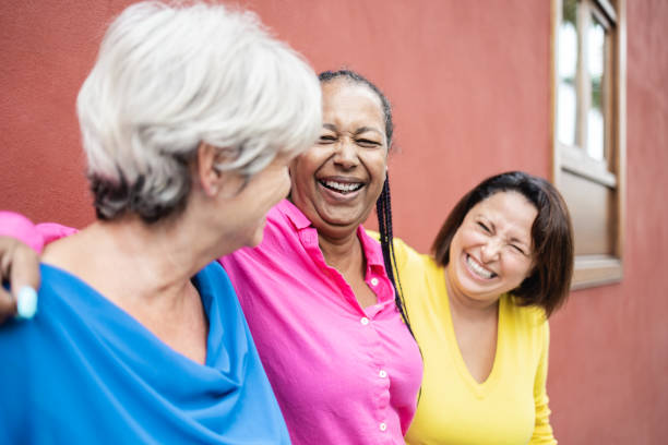 Multiracial happy senior women having fun hugging together outdoor - Elderly friendship people concept stock photo