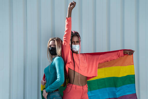 multiraciale lesbische vrienden met masker dat een lgbt regenboogvlag houdt - nadruk op gezichten - gay demonstration stockfoto's en -beelden