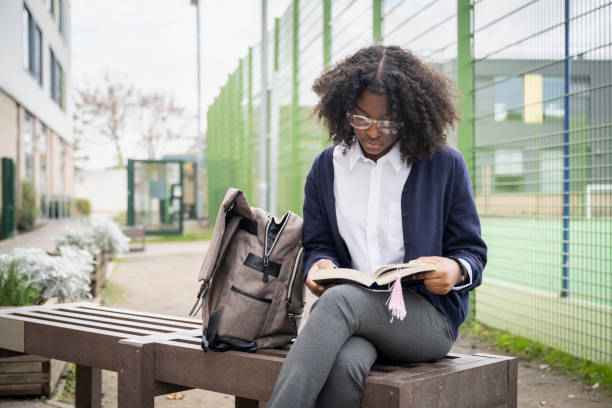 Multiracial schoolgirl reading a book on campus before class stock photo