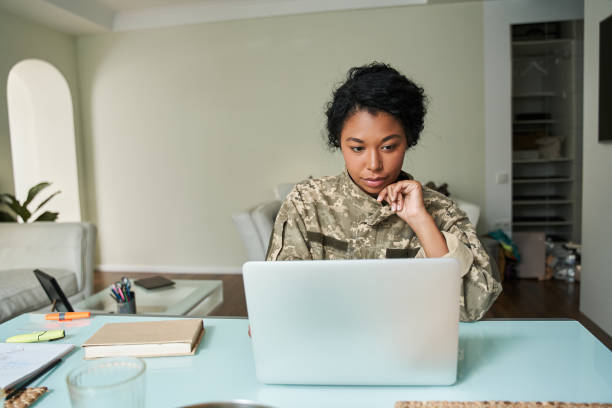 Multiracial soldier woman wearing military uniform looking at the laptop screen stock photo