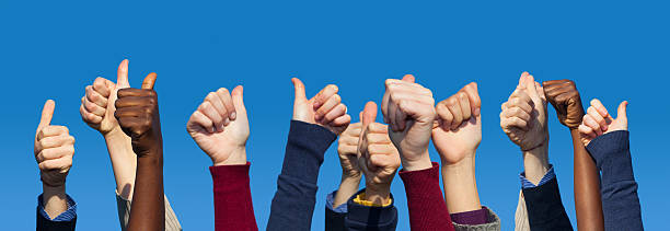 Multiracial Thumbs Up Against Blue Sky stock photo