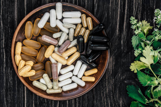 Multivitamin pills on a clay plate, on a vintage wooden table, with a sprig of mint stock photo