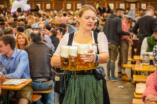 Munich, Germany, Oktoberfest, waitress in tyrolean costume holding beers, tent interior background