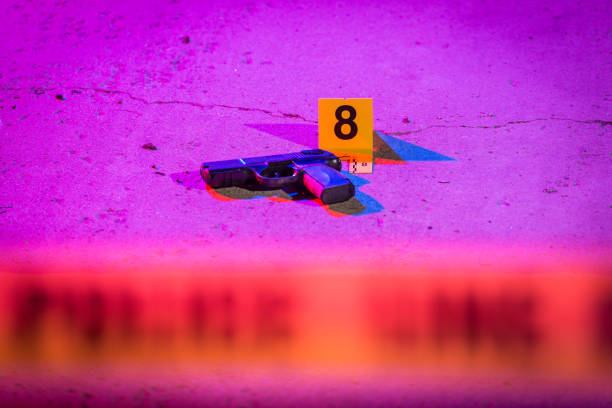 Murder Weapon A black handgun lays on the pavement in a crime scene, marked with an evidence marker. gun violence stock pictures, royalty-free photos & images