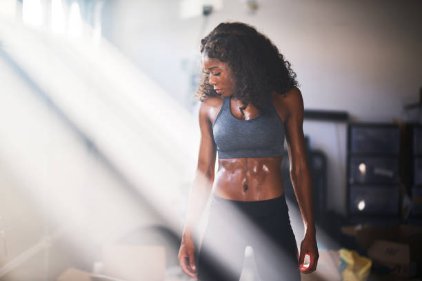 muscular african american woman sweating from work out in home gym muscular african american woman sweating from work out in home gym with light rays body building stock pictures, royalty-free photos & images