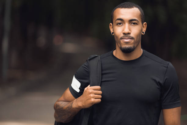 Muscular african-american man posing outside after workout Muscular african-american man wearing black t-shirt and backpack posing outside after workout athleticism stock pictures, royalty-free photos & images