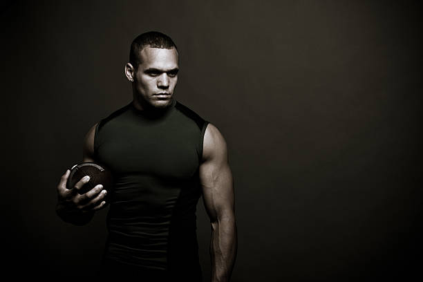 Muscular man in black tank top holding a football stock photo