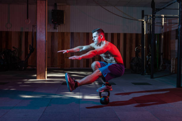 Muscular man squat with one leg while standing on a kettlebell in neon red blue gradient light.