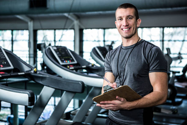 Muscular trainer writing on clipboard Muscular trainer writing on clipboard at the gym athleticism stock pictures, royalty-free photos & images