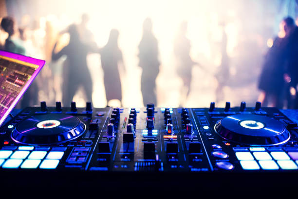 music controller DJ mixer in a nightclub at a party music controller DJ mixer in a nightclub at a party against the background of blurred silhouettes of dancing people club dj stock pictures, royalty-free photos & images