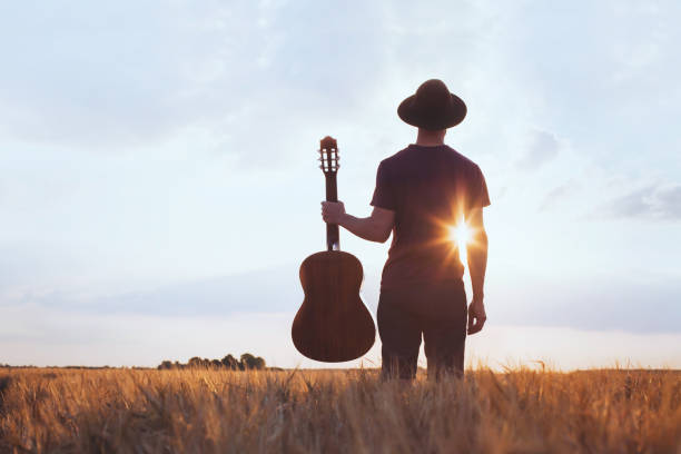 music festival background, silhouette of musician artist with acoustic guitar music festival background, silhouette of musician artist with acoustic guitar at sunset field country and western music stock pictures, royalty-free photos & images