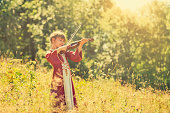 Little girl in dress playing violin on sunny meadow.