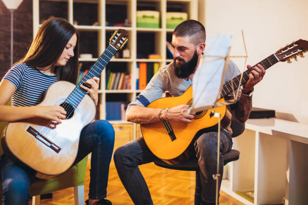 Music teacher tutoring young girl to play guitar at home stock photo