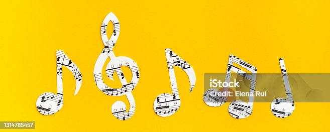 istock Musical notes and clef cut from paper with musical text in a row on yellow background. Web banner 1314785457
