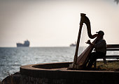 Vancouver, Canada - June 26,2009 : Musician harpist performer silhouette sit on a bench near the sea in Vancouver, Canada