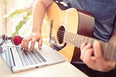Musician playing acoustic guitar and recording music on computer or learning fom online lesson