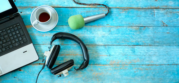 Music,podcast or audiobook concept, flat lay with headphones, microphone, coffee and laptop on blue wooden table stock photo
