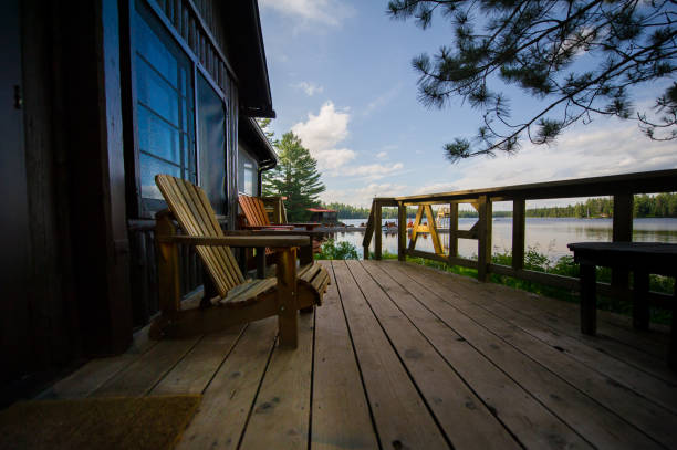 Muskoka chairs on a wooden deck Two Muskoka chairs on a wooden deck facing a lake. In the background there’s a pier with a big amount of chairs cottage stock pictures, royalty-free photos & images