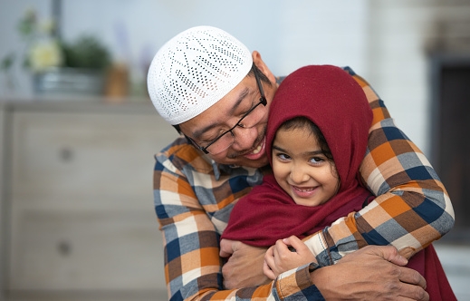 An adorable Muslim little girl is being embraced by her father. She appears to be smiling and happy.