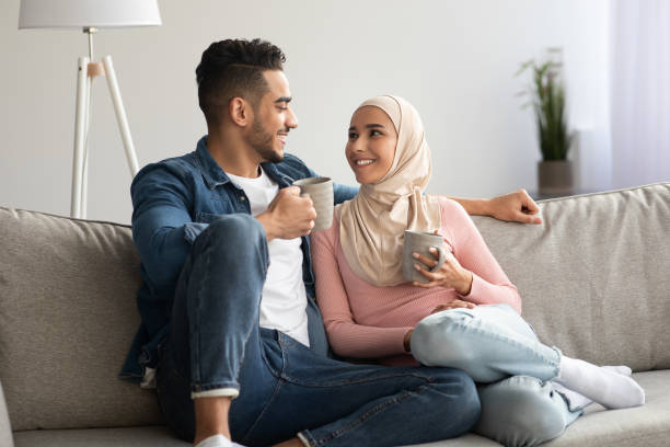 Muslim lovers drinking tea and talking at home Lovers young man and woman in hijab drinking tea and talking at home. Beautiful muslim couple drinking coffee while sitting on sofa at living room, spending weekend together, copy space hot middle eastern women stock pictures, royalty-free photos & images