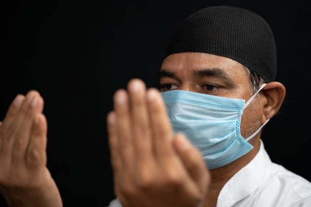 uomo musulmano in maschera medica preformando salah o la preghiera chiudendo gli occhi. - salah foto e immagini stock