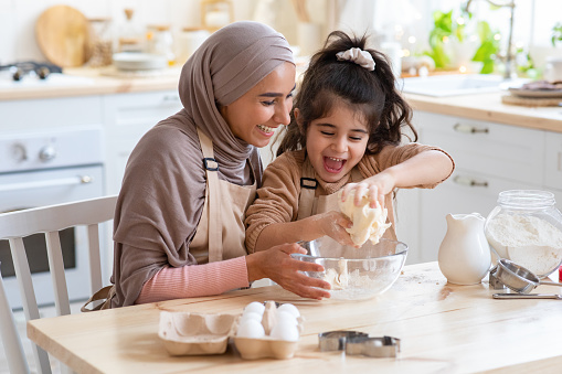 Cheerful Muslim Mom In Hijab And Her Little Daughter Having Fun At Home, Baking Pastry In Kitchen Together, Kneading Dough While Preparing Cookies, Enjoying Cooking Homemade Food. Closeup Shot