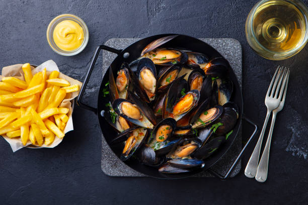 Mussels with french fries and white wine in cooking pan. Grey background. Top view. Mussels with french fries and white wine in cooking pan. Grey background. Top view. belgian culture stock pictures, royalty-free photos & images