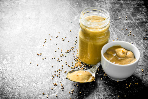 Mustard in a glass jar, spoon and bowl. stock photo