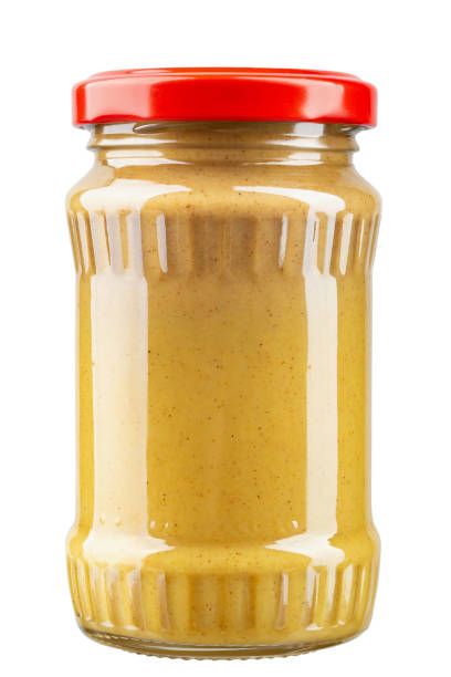 Mustard in a transparent glass jar with a closed red metal lid isolated on white background. stock photo