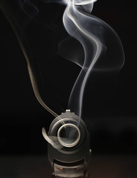 muzzle smoke looking down the barrel of a just-fired hand gun, smoke curling from the muzzle. Black gun, black background Smoking Kills stock pictures, royalty-free photos & images