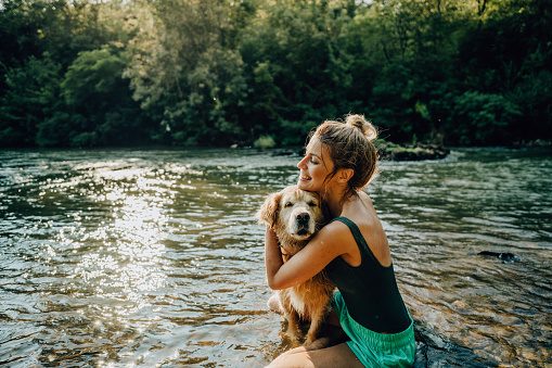 Photo of a young woman and her dog bathing in the river; enjoying the beautiful, warm summer afternoon far from the hustle of the city.