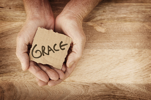 Grace written on small piece of cardbord held in hands over wood background