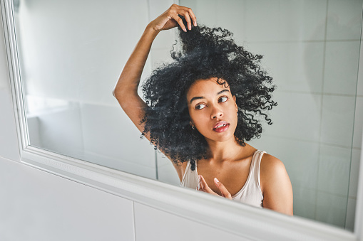 Shot of an attractive young woman styling her hair in the bathroom mirror at home